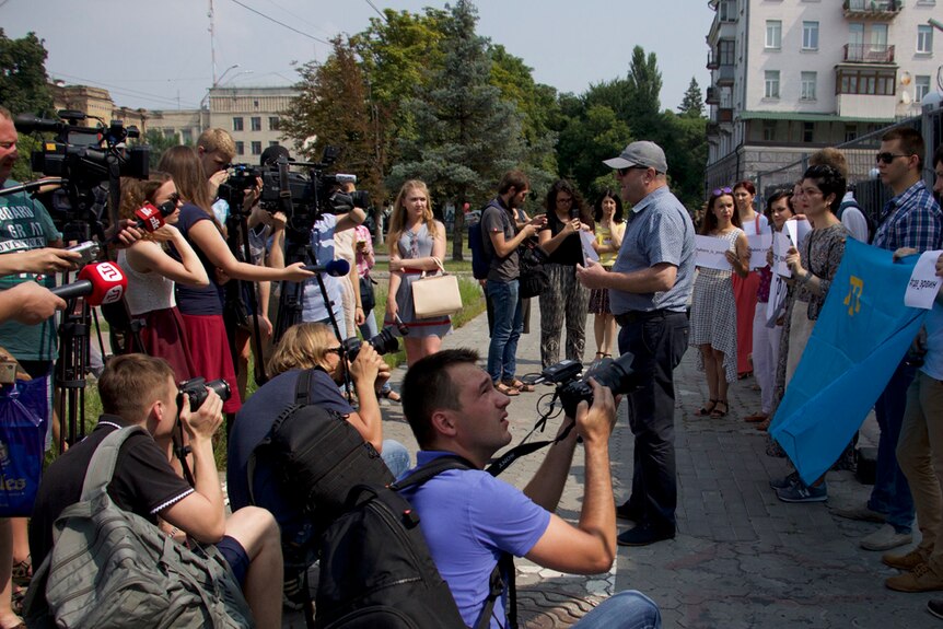 Protestor Riza Shevkhiev is surrounded by journalists holding cameras and microphones at a protest in Kiev.