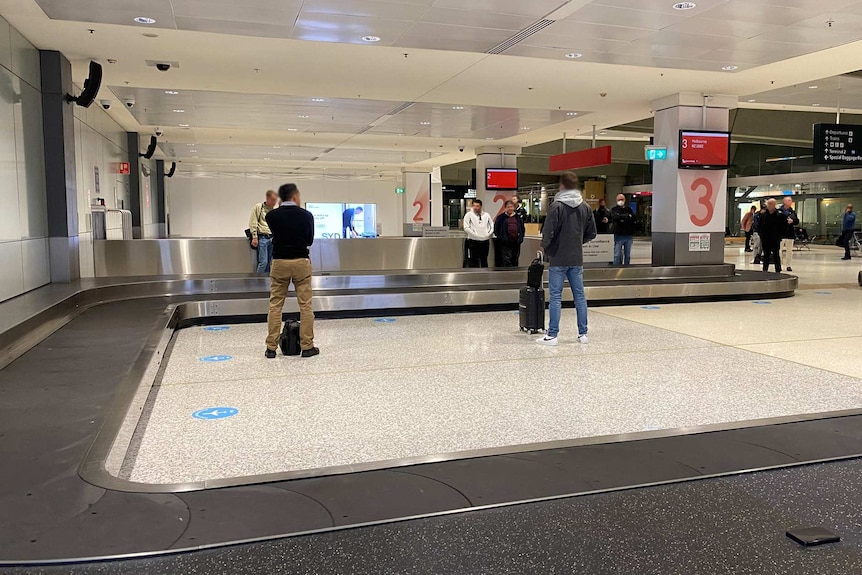 Photo of people social distancing in a luggage pickup area of an airport.