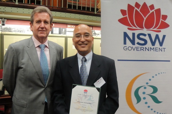 Two men stand in front of NSW government banner.