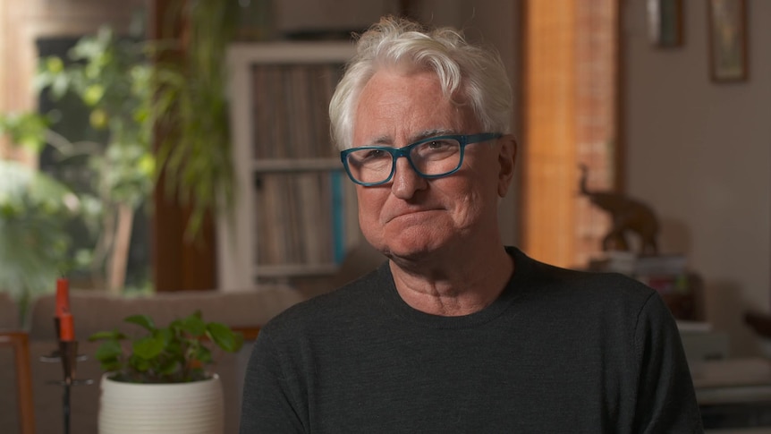 A man with grey hair, glasses and wearing a black top.