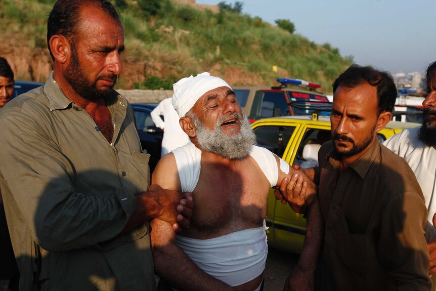A man is being supported by two men on either side as he mourns/cries