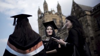 Three university graduates stand in front of a stone building.