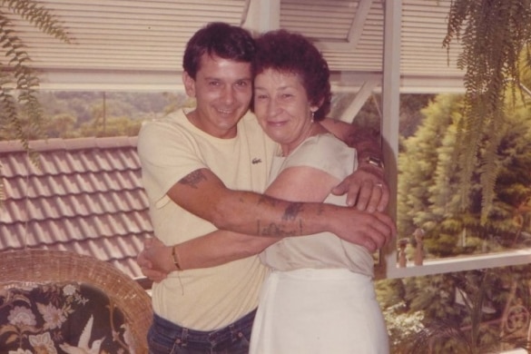 Faded colour photo of younger man and older woman hugging each other tightly and smiling widely.