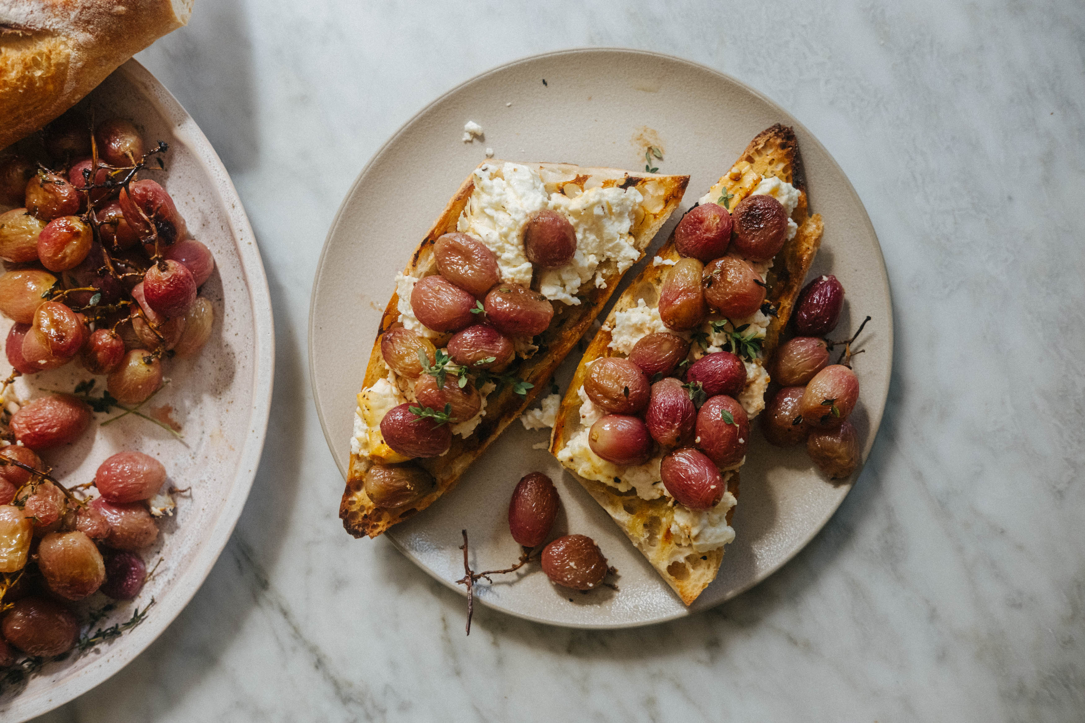 A block of feta cheese and red grapes, roasted on a tray with thyme to create a simple meal when served with a baguette