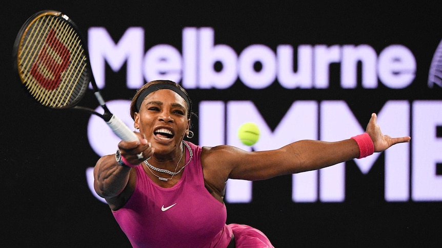 A tennis player grimaces as she reaches to hit a forehand return during a match.