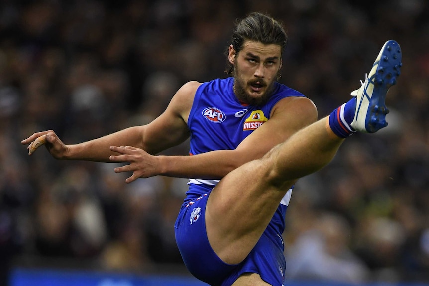 A Western Bulldogs AFL player watches the ball after kicking it, with his right leg in the air.
