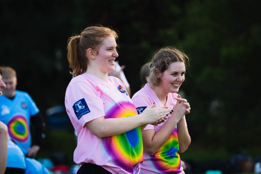 Two people wearing pink t-shirts smile and clasp their hands together,