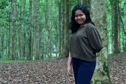 A woman standing in a forest surrounded by trees.