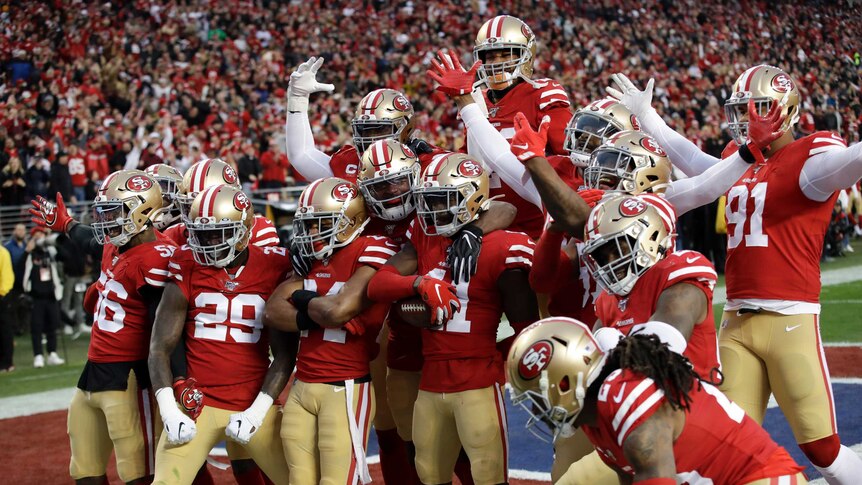 A large group of 49ers players stand in a huddle posing for photographers mid-match.
