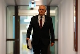 Morrison strides down an empty corridor holding a folder