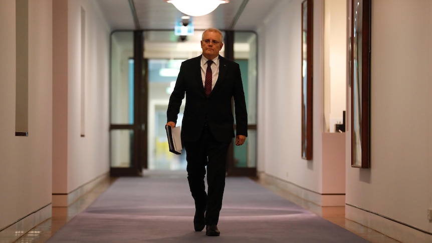 Morrison strides down an empty corridor holding a folder