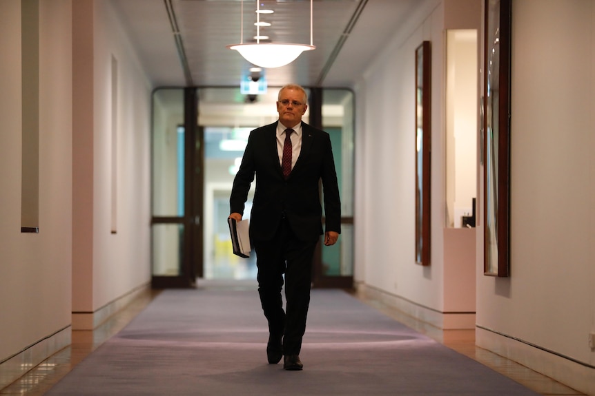 Morrison strides down an empty corridor holding a folder