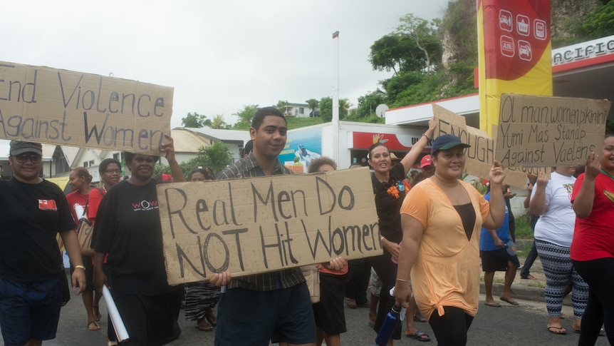 A man holds a banner that reads "real men do not hit women"