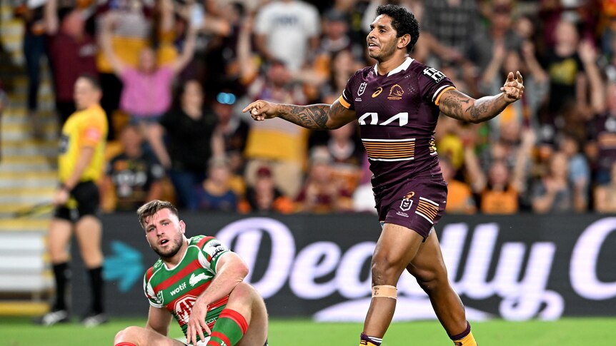 A Brisbane Broncos NRL players celebrates a try as a South Sydney opponent looks on.