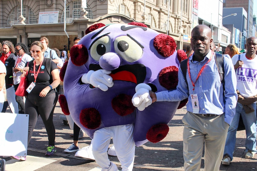 A person wearing the costume of large purple sphere with red spots and a face walks down a street in Durban.