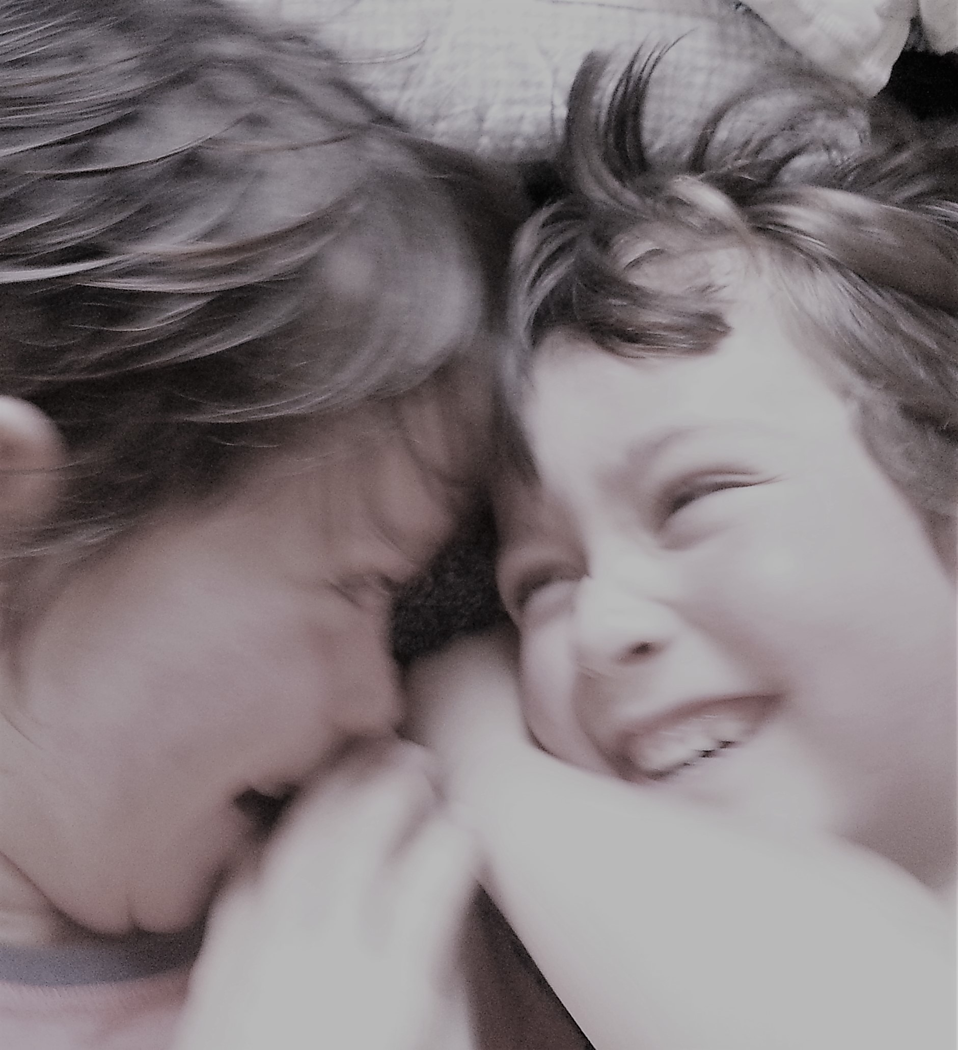 Two young boys with their faces together, laughing.