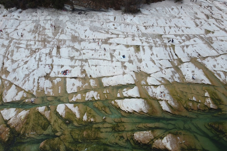 an aerial view of white rock exposed on Lake Garda with people sunbathing on it