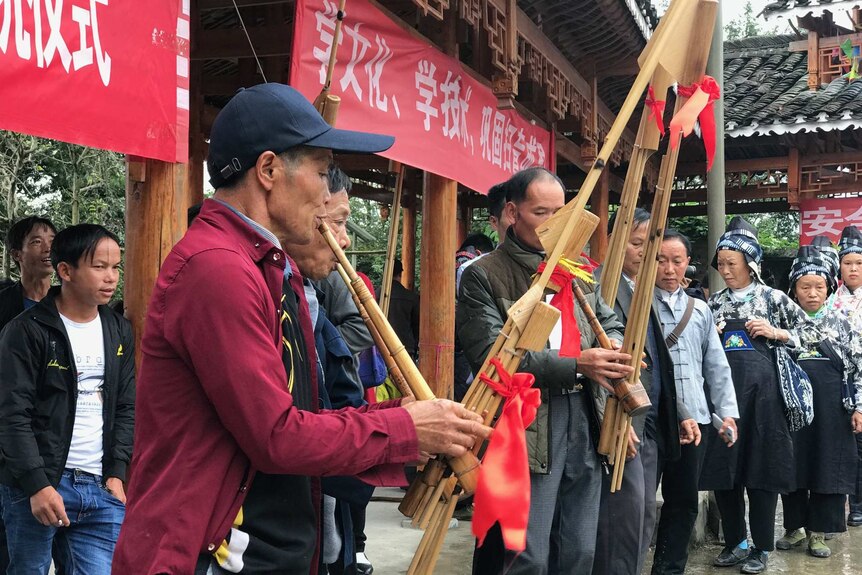 Chinese villagers play traditional instruments underneath red and white banners.