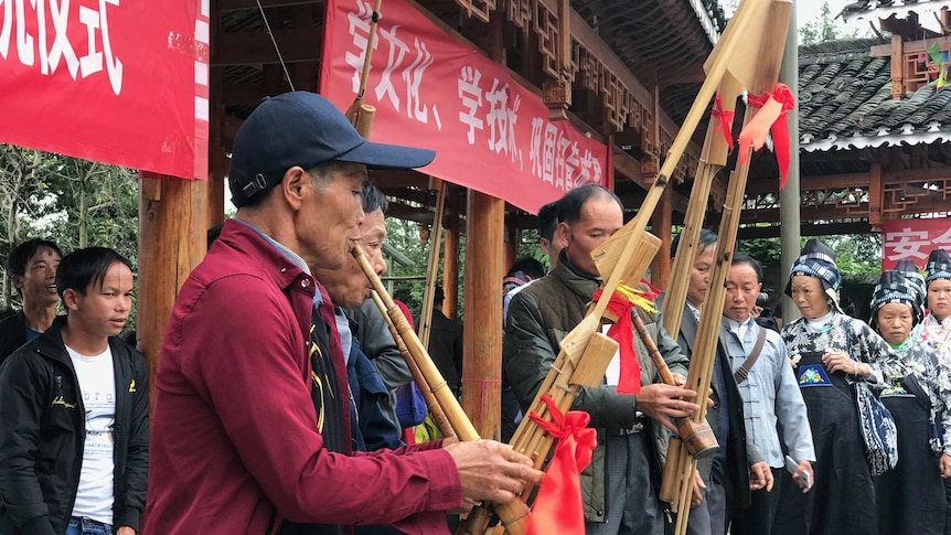 Chinese villagers play traditional instruments underneath red and white banners.