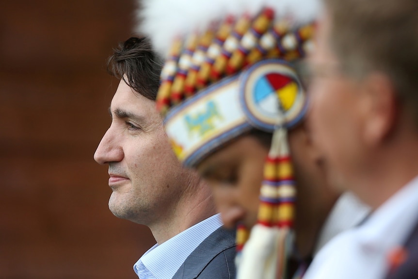 Canadian Prime Minister Justin Trudeau sits next to an Indigenous man wearing a headdress.