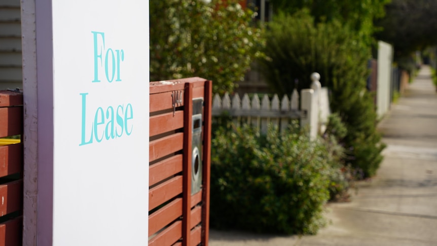 Close up of a white for lease sign with blue writing attached to a wooden fence