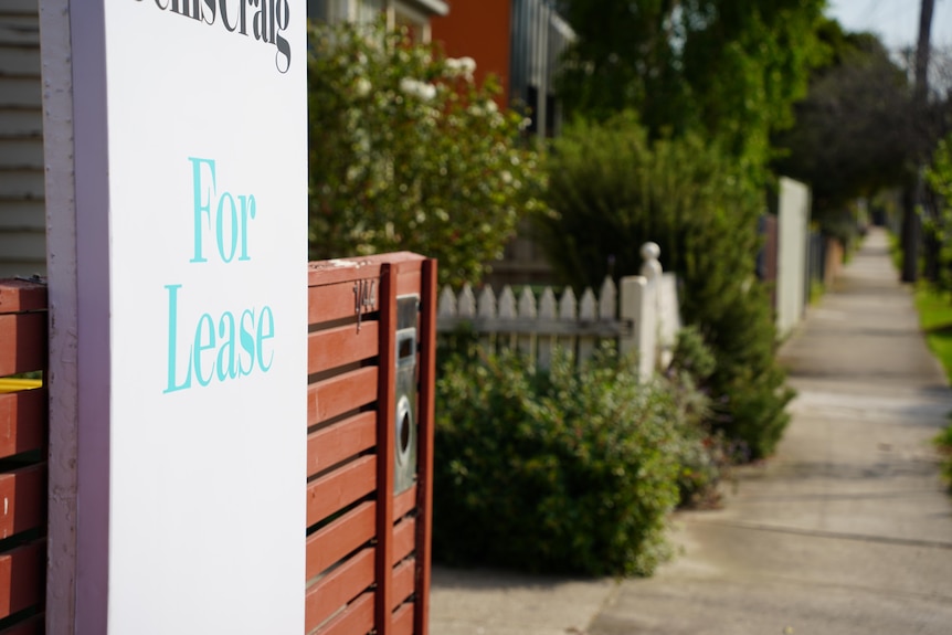 Close up of a white for lease sign with blue writing attached to a wooden fence