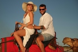 Man and woman ride on a camel on Cable Beach in WA.