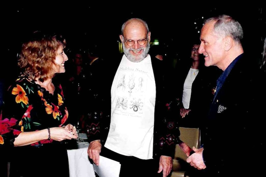 Two men and a woman chatting at a night function.