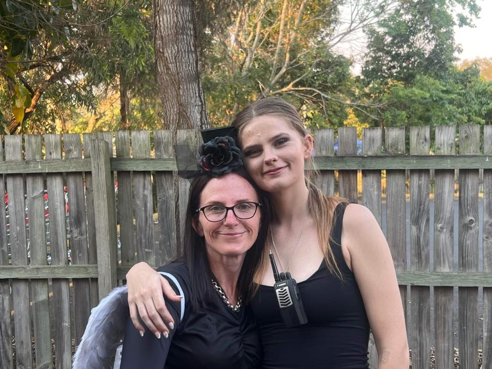 A woman with a flower fascinator hugging her taller daugher