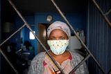 A woman in a face mask looks through a barred window