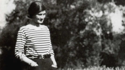 A woman in a striped top stands, hands in pant pockets, next to a dog. (Dog out of frame in some crops)