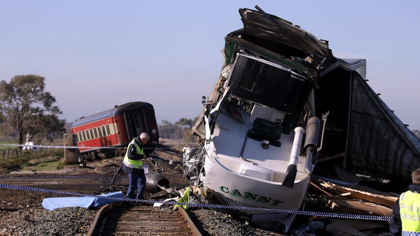 An emergency worker stands on the tracks next to a mangled truck and in front of a derail train carriage.