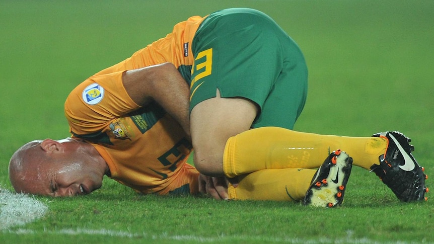 Australia's Mark Bresciano holds his knee after injuring it in the 2-2 draw with Oman at Sydney's Olympic stadium.