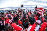 A group of African men wearing red tops hold a trophy up