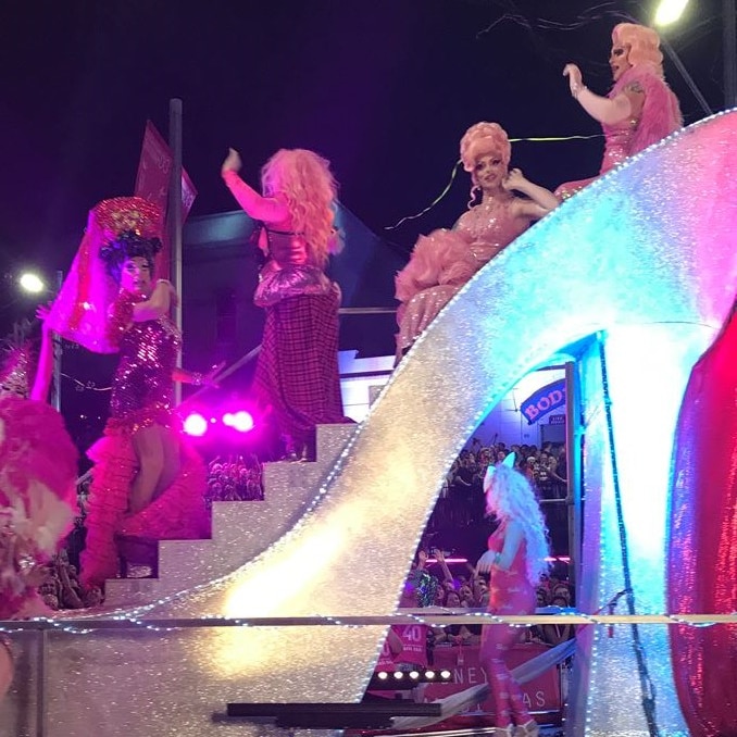 People celebrating Mardi Gras stand on a float shaped like a high heel.