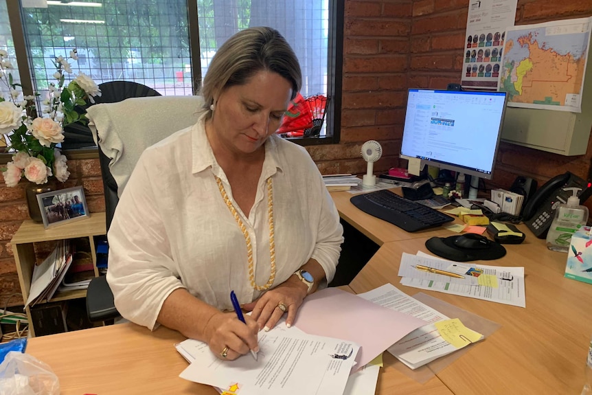 Ingrid Stonhill sits at her desk in an office signing a piece of paper.