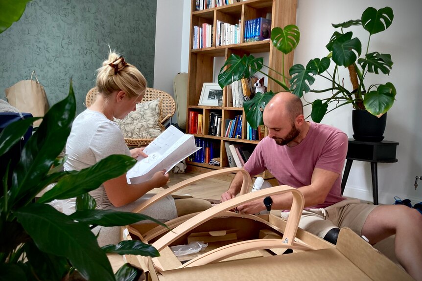 A woman and a man construct a piece of wooden furniture.