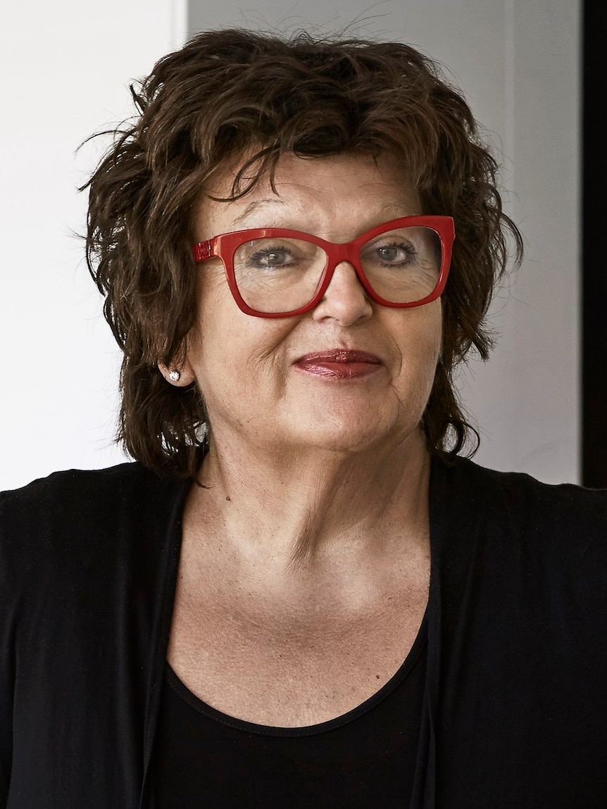 a middle aged woman with dark, short hair and red glasses smiles at the camera.