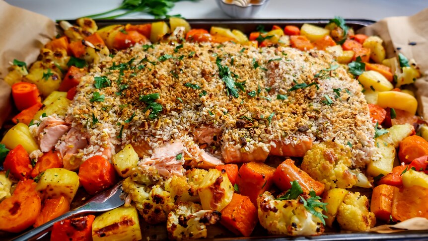 Baked salmon fillets with a pistachio crumb atop roast vegetables (potato, carrots, cauliflower) on a baking tray.