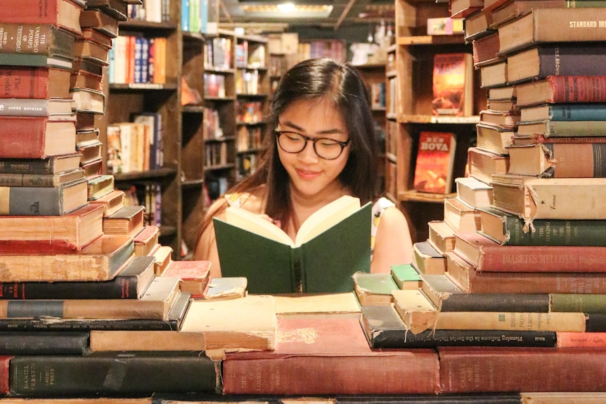 Woman reading book, surrounded by books