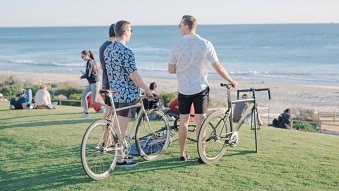 Three men look out to the ocean while holding their commuter bikes