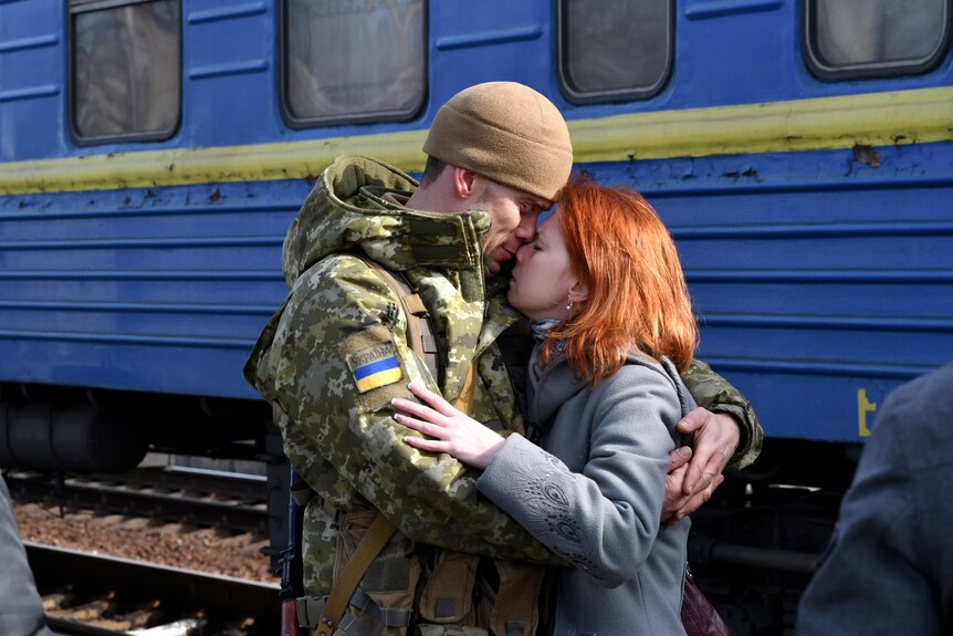 A Ukrainian man in a military uniform embraces a woman in front of a train.