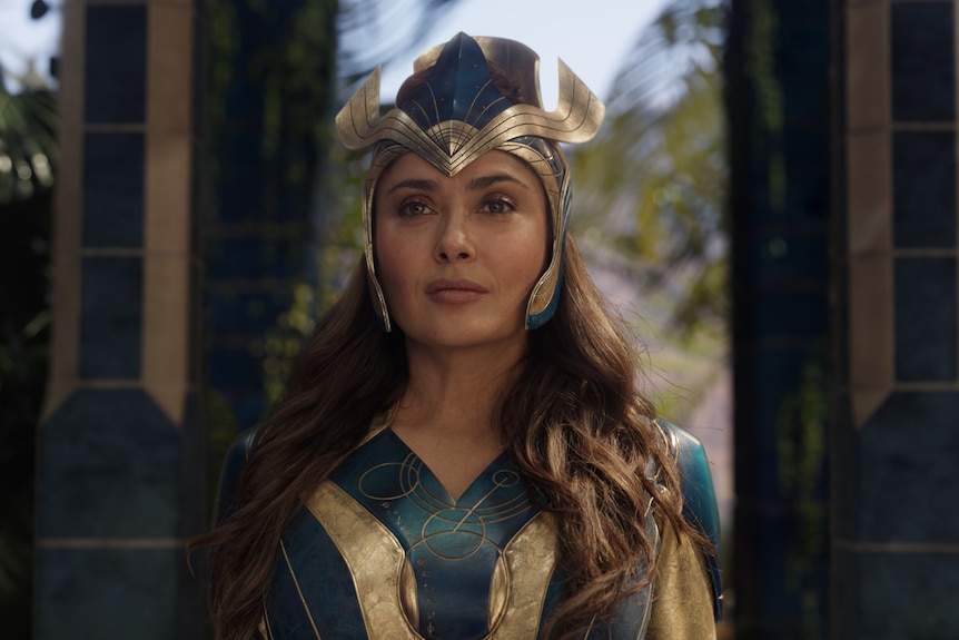 Salma Hayek in a dark blue and gold superhero costume, including an ornate headdress, has a determined expression