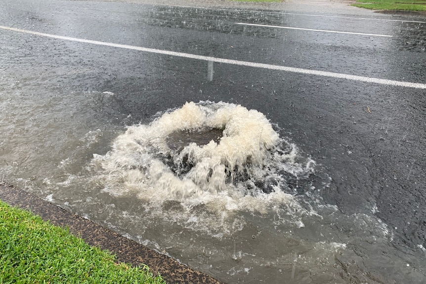 A man hole cover with water gushing out from underneath