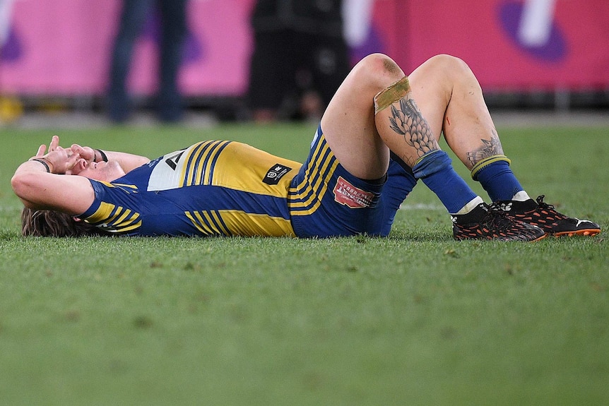 A Parramatta Eels NRL player lies on the ground with his hands on his forehand after the loss to South Sydney.
