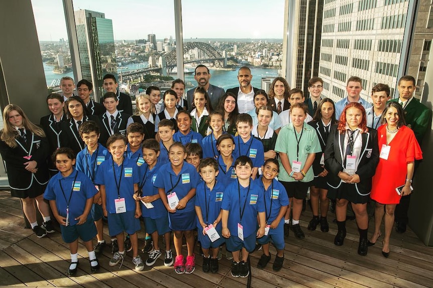 School children stand with Adam Goodes and Michael O'Loughlin with the Sydney Harbour Bridge in the background.