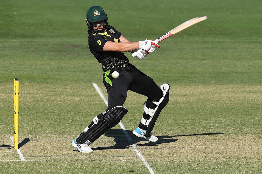 An Australian female T20 cricketer wearing a helmet plays a cut shot to her right against New Zealand in Brisbane.