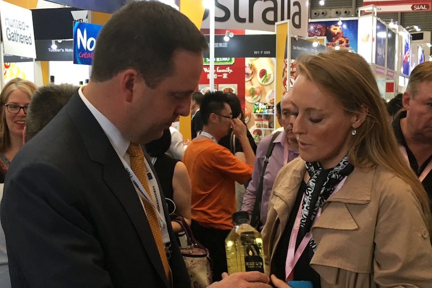 A woman and a man standing in a crowded indoor space looking down at a bottle of canola oil