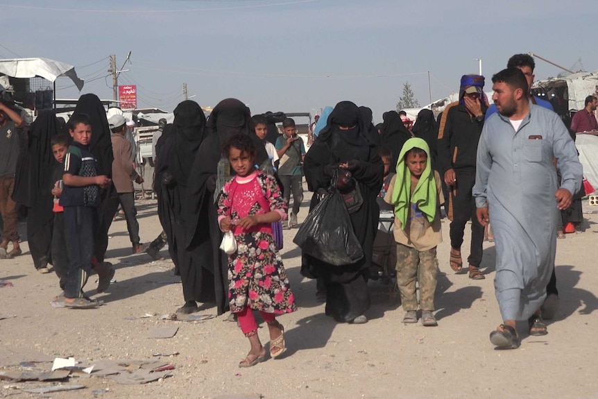 Children seen walking on a dirt road near makeshift buildings.