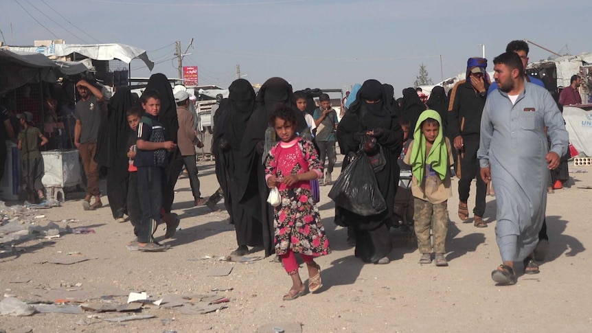Children seen walking on a dirt road near makeshift buildings.